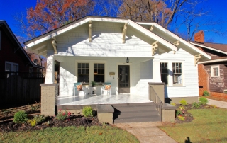 White shingle home with brown details brown front door brown trim windows front porch with sitting area brown steps to front porch flowers planted around the front