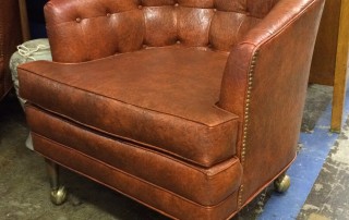 Brown leather club chair with brass studs on wheels