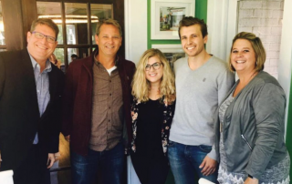 Two women and three men standing together with their arms around each other